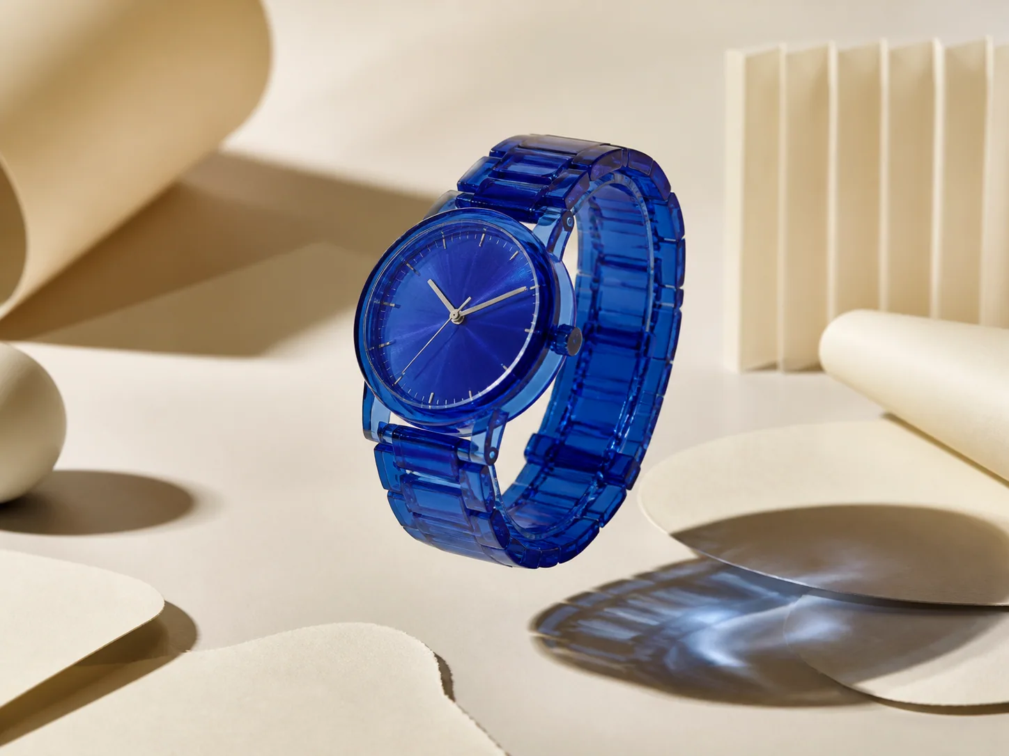 A cobalt watch floating above sculptural cream paper forms